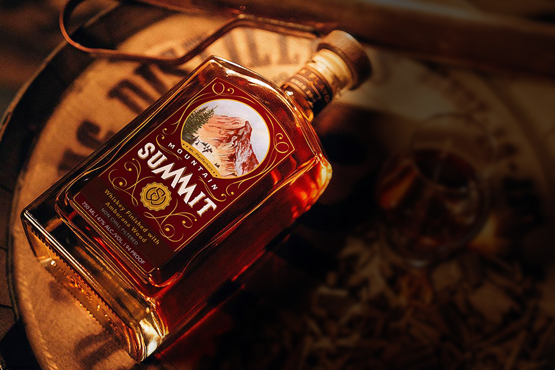 Mountain Summit: Ambruana Finished Whiskey Bottle - Professionally photographed. Sitting atop an aging barrel with a glass next to it.